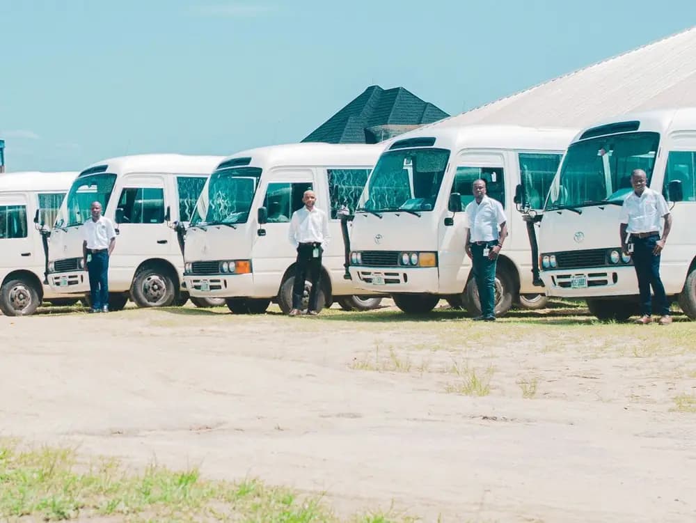 Des chauffeurs en chemise blanche, chacun devant son minibus, sur le parc de l'entreprise